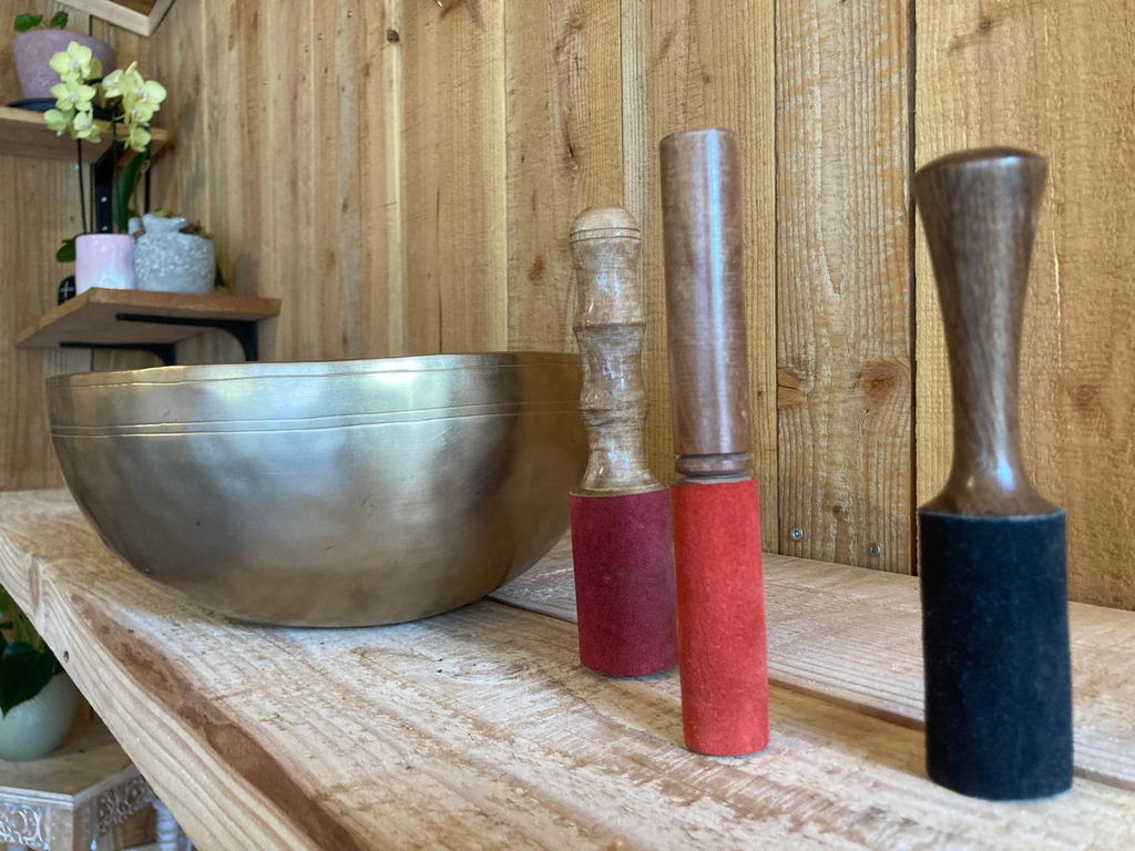 Grand bol chantant tibétain et trois maillets gainés de feutre rouge et noir, sur une planche de bois