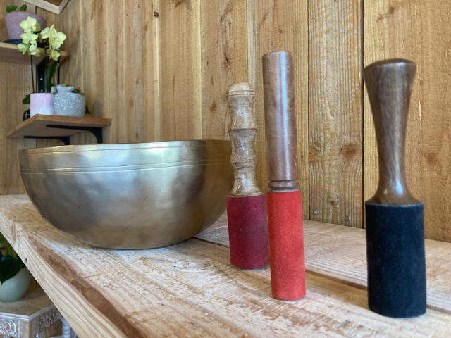 Grand bol chantant tibétain et trois maillets gainés de feutre rouge et noir, sur une planche de bois