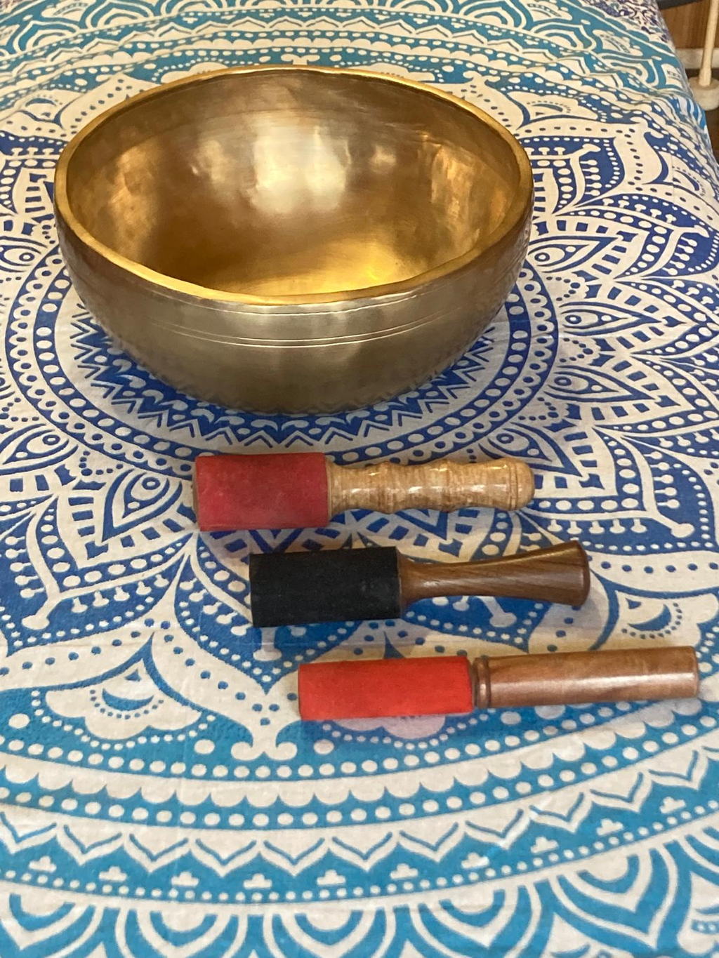 Bol chantant tibétain et trois maillets posés sur un tissu mandala bleu et blanc, vus du dessus