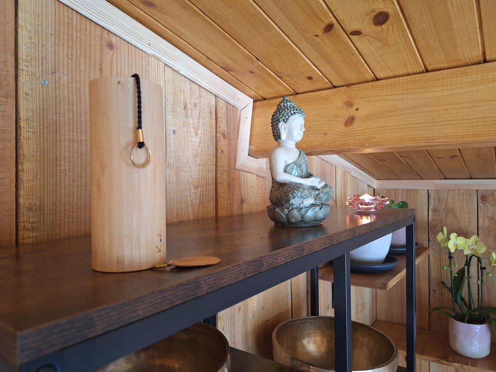 Statue de Bouddha et bougie allumée sur une console en bois, bols chantants en dessous