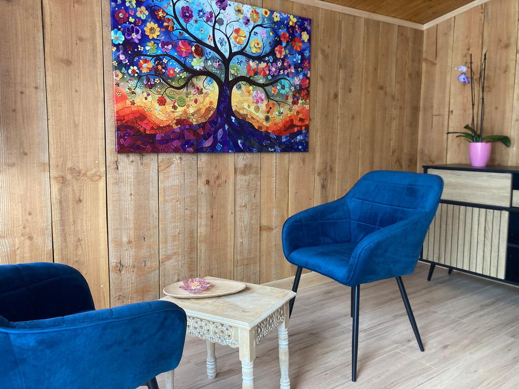 Le coin accueil du chalet : deux fauteuils en velours bleu autour d'une petite table sculptée, sous un tableau arbre de vie