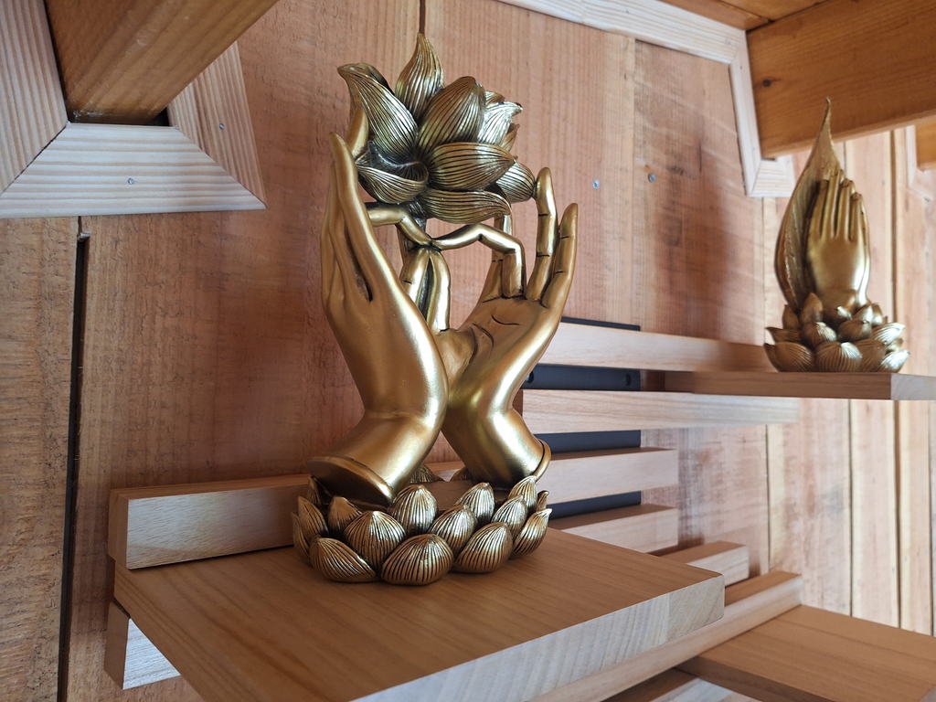 Sculpture dorée de deux mains ouvertes tenant une fleur de lotus