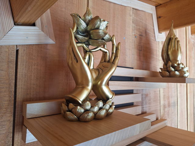 Sculpture dorée de deux mains ouvertes tenant une fleur de lotus