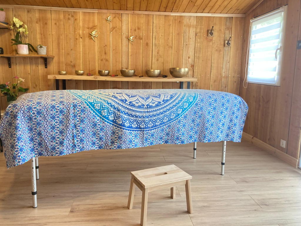 Vue d'ensemble de la salle de soin en bois, table recouverte d'un tissu mandala et rangée de bols chantants au mur