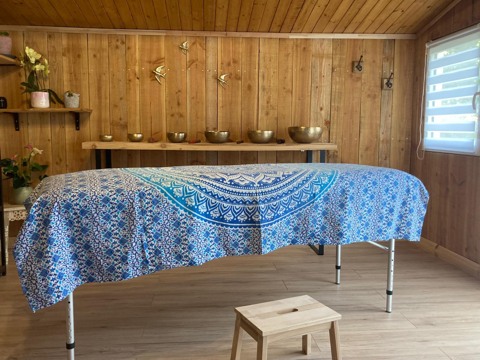 La salle de soin du chalet : table de massage recouverte d'un tissu mandala bleu, bols chantants alignés sur l'étagère du fond