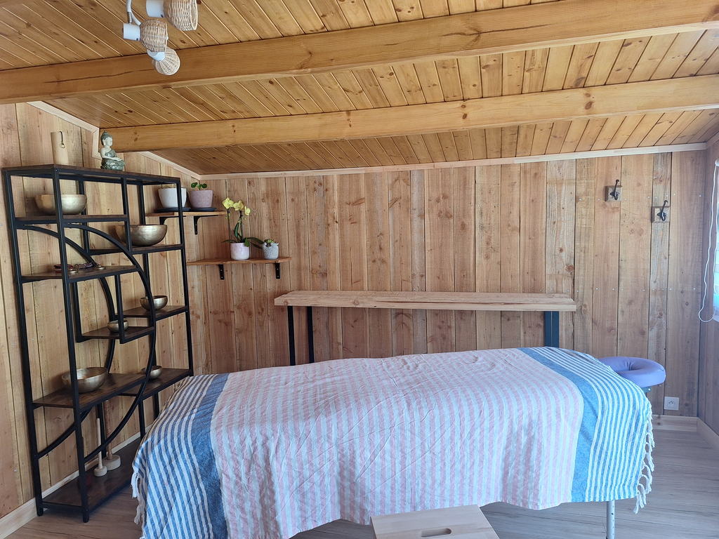 Table de massage recouverte d'un plaid rayé, face à une étagère de bols chantants