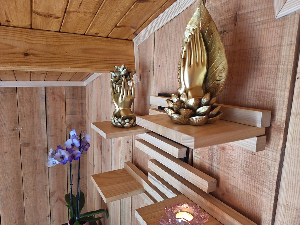 Statuettes dorées en forme de mains posées sur des étagères de bois, près d'une bougie
