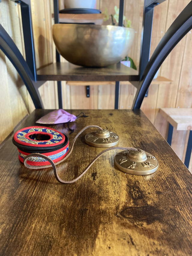 Cymbales tibétaines tingsha et leur étui brodé rouge et or sur une étagère en bois, un bol chantant au-dessus